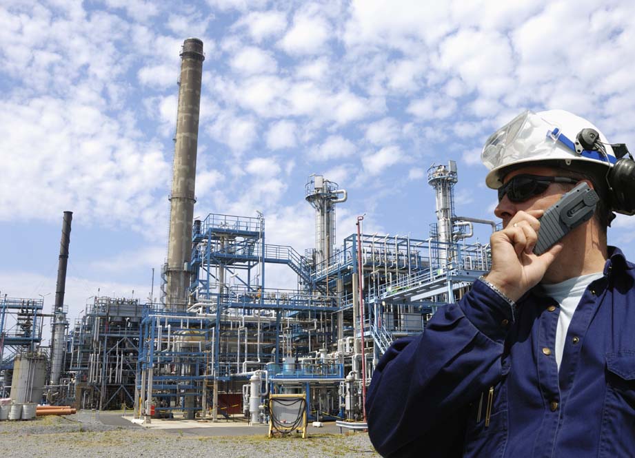 engineer talking in mobile-phone, large oil refinery in the back